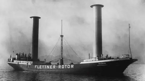 Hulton Deutsch/Getty Images Black and white photo showing the Buckau with its two modified rotating towers and a mast in the middle. It now contains the words "Flettner-Rotor" on the sides.