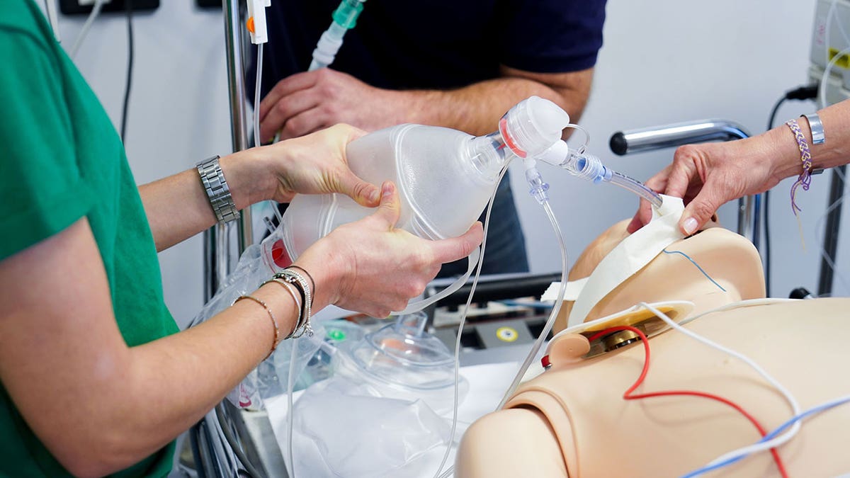 Medical professionals practice artificial respiration on a training mannequin in a hospital setting.
